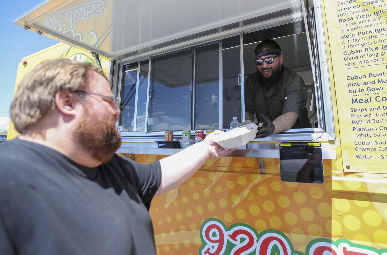 Zack Cookle hands off an order to Daniel Lehman on May 8 at Consign It! in Green Bay. Cookle owns and operates the Rollin Cubanos food truck.