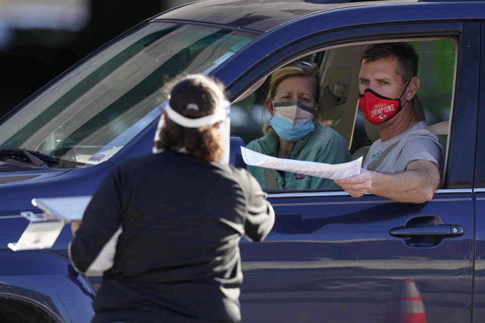 FILE - In this Nov. 3, 2020, file photo, a man hands his completed ballot to an election worker at a drive-thru polling location in Kansas City, Mo. Poll workers in some states who came in contact with voters on Election Day are now reporting they have tested positive for the coronavirus despite painstaking efforts to secure election sites. To be sure, the cases cannot be tied definitely to polling places. (AP Photo/Charlie Riedel, File)