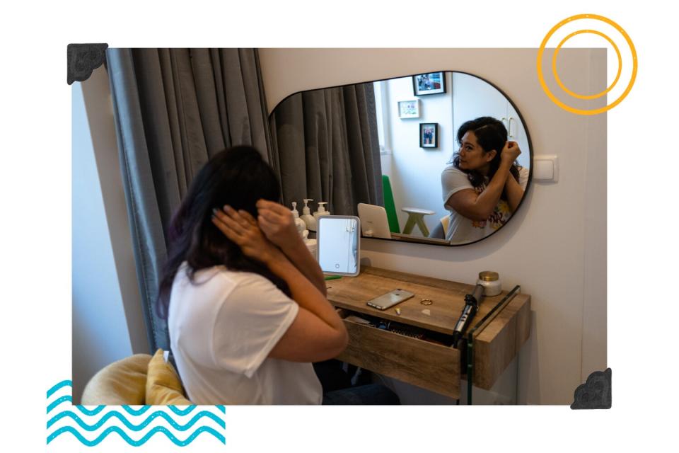 a woman fixes her hair in front of a mirror.