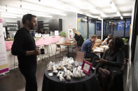 In this Tuesday, Nov. 5, 2019 photo, Lanny Grossman, left, owner of public relations firm EM50 Communications, talks with pastry chef Asia Bullock about her Sweet Treats business at a WeWork office space, in New York. WeWork is slashing the lavish spending that has fueled its breakneck growth while racking up unsustainable losses. Experts are skeptical that the office-sharing company can achieve meaningful cost reductions without somehow squeezing tenants. (AP Photo/Mark Lennihan)