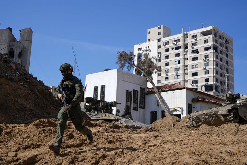 Un soldado israelí corre por un agujero similar a un cráter que da paso a una pequeña entrada de túnel en el complejo del OOPS, en Gaza, febrero de 2024