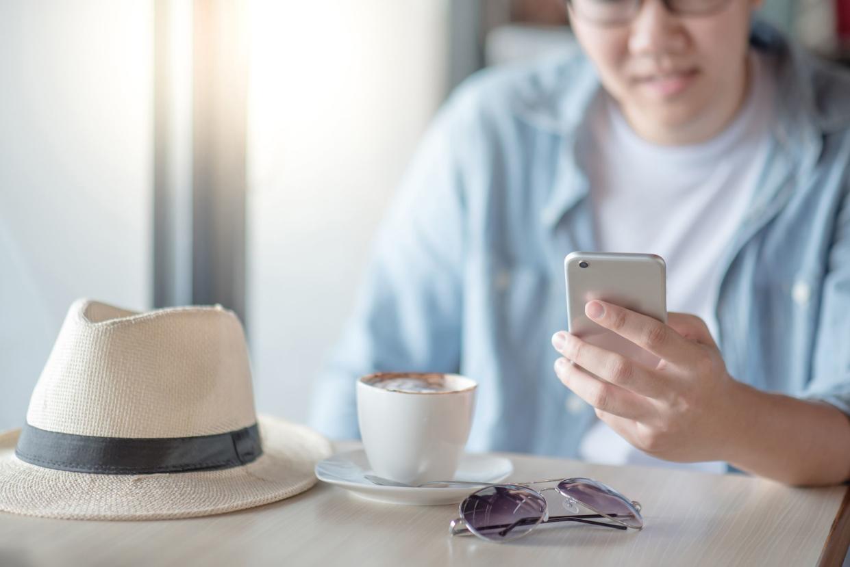 Asian man using smartphone while drinking coffee in the cafe. Relaxing time with entertainment and social media mobile app. Modern device for global communication.  Internet of things concept