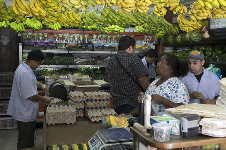 A customer selects bananas as others buy goods at a fruit and vegetable store in Caracas, July 10, 2015. REUTERS/Marco Bello