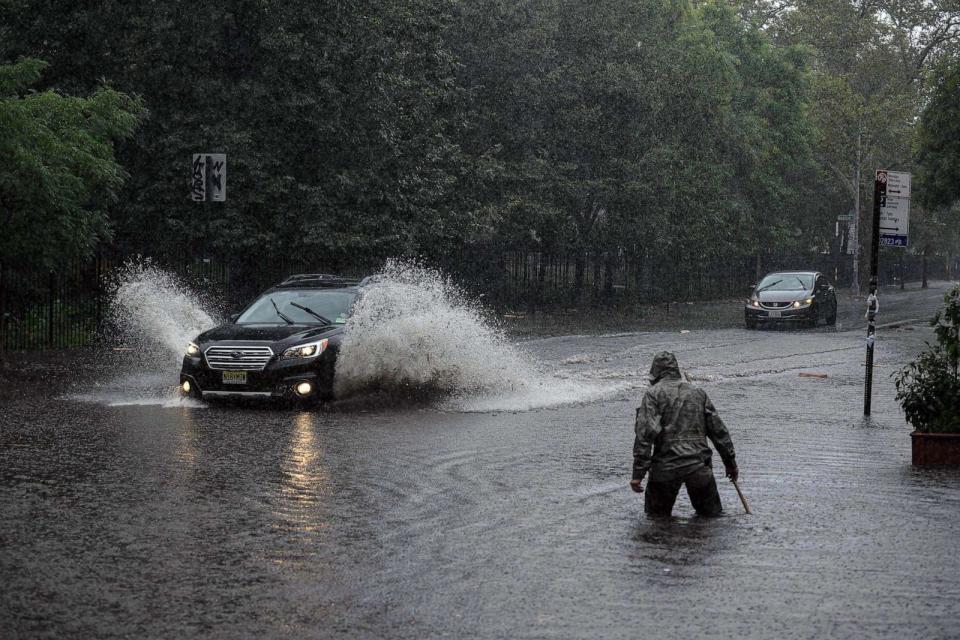 PHOTO: A man clears debris from a drain as a car make their way through floodwater in Brooklyn, New York, Sept. 29, 2023. (Ed Jones/AFP via Getty Images)