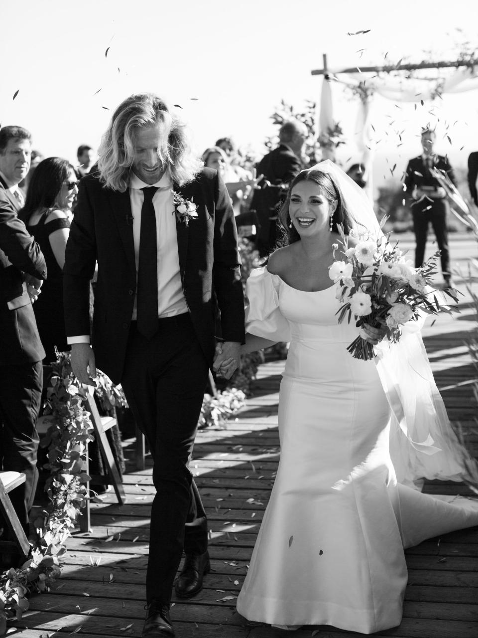 A black and white shot of a bride and groom hold hands as they exit their wedding ceremony.