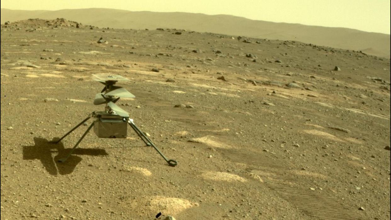  A small helicopter sits in red rocky dirt. 