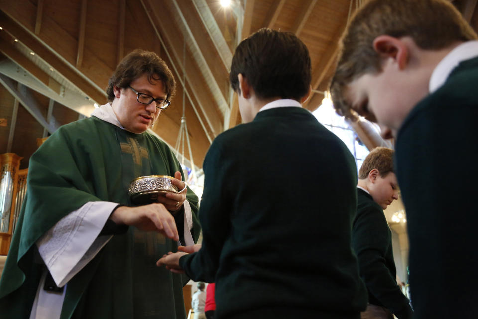 In this Feb. 7, 2020, photo, converted Catholic Priest Joshua Whitfield of north Dallas, left, gives communion during a weekly student Mass at St. Rita Catholic Community in Dallas. Whitfield came to the Catholic church as a former Episcopalian pastor, a husband and soon-to-be dad. (AP Photo/Jessie Wardarski)