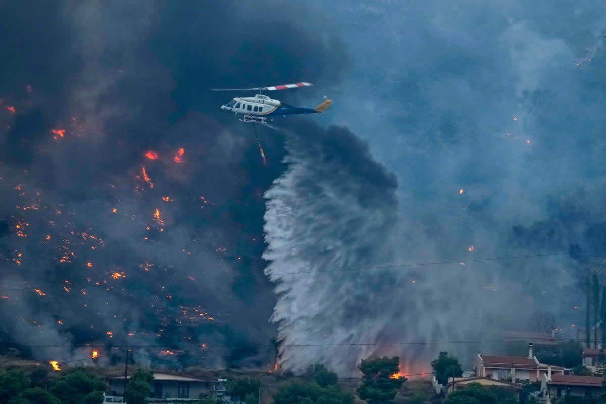 A firefighting helicopter dumps water as fire approach houses in Kalamaki near Agioi Theodori about 60 Kilometres west of Athens , on Monday, July 17, 2023. (AP)