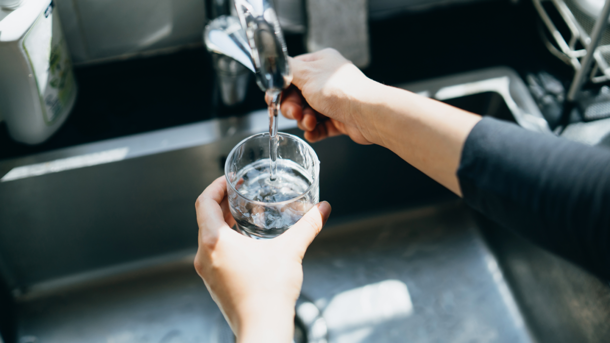 A glass being filled with water over a sink