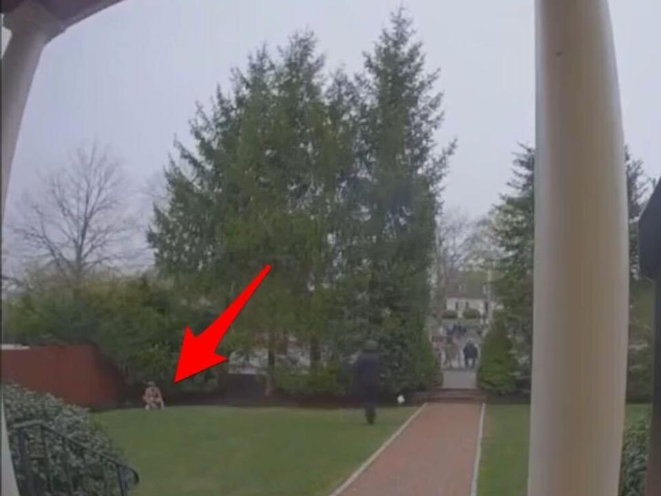 screenshot from @BabzOnTheMic's tweet including the video, showing a person in the far left corner squatting on the yard and a red arrow (added by Insider) pointing to them.