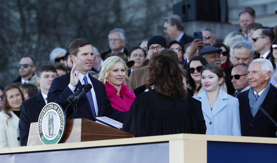 Gov. Andy Beshear raised his right hand as he was sworn in during his inauguration on the steps of the Kentucky State Capitol building in Frankfort, Ky. on Dec. 13, 2023. HIs wife, Britainy Beshear, and other family members were at right.