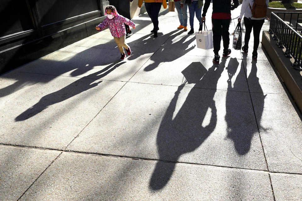 Shoppers cast their shadows Saturday, Nov. 28, 2020, as they walk Chicago's famed Magnificent Mile shopping district while a young kid runs by. (AP Photo/Charles Rex Arbogast)