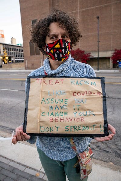 Decrying the insidiousness of white supremacy at a protest march. <a href="https://www.gettyimages.com/detail/news-photo/woman-wearing-a-mask-holds-a-sign-likening-covid-19-to-news-photo/1229553338?adppopup=true" rel="nofollow noopener" target="_blank" data-ylk="slk:Stephen Zenner/SOPA Images/LightRocket via Getty Images;elm:context_link;itc:0;sec:content-canvas" class="link ">Stephen Zenner/SOPA Images/LightRocket via Getty Images</a>