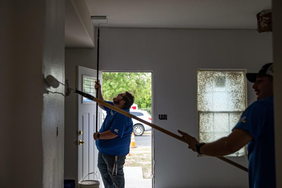 Best Buy employees Ryan Padilla, back, and Canek Villarreal, front, paint the living room and hall of a two-bedroom, one-bathroom home while volunteering for Habitat for Humanity on May 19, 2022, in Corpus Christi, Texas.