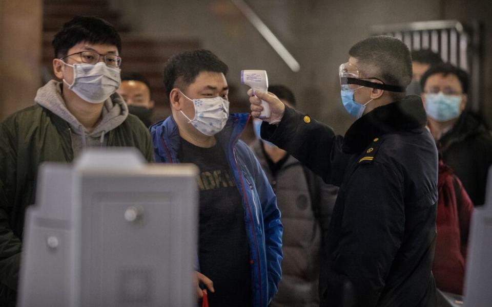 A Chinese passenger that just arrived on the last bullet train from Wuhan to Beijing is checked for a fever by a health worker at a Beijing railway station. | Kevin Frayer/Getty Images