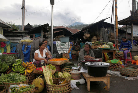 Mount Agung volcano erupts behind as women as the sell food in the morning market in Culik, Karangasem Regency, Bali, Indonesia, November 29, 2017. REUTERS/Darren Whiteside