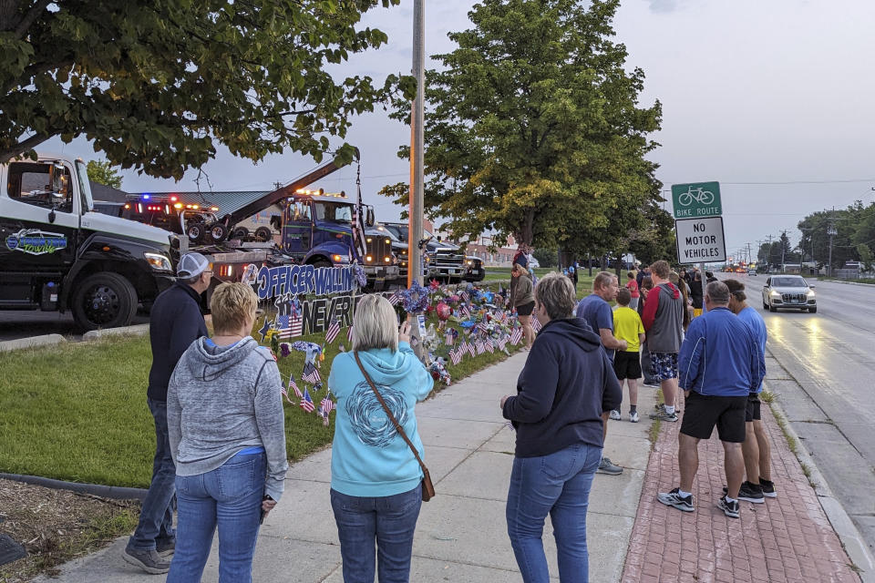 People gather at the memorial site for fallen Fargo Police Officer Jake Wallin on Saturday, July 22, 2023, in Fargo, N.D., hours before Wallin's funeral service in Pequot Lakes, Minn. Wallin was killed July 14 when a man armed with 1,800 rounds of ammunition, multiple guns and explosives began firing on officers who were responding to a traffic crash. (Ryan Janke/KFGO via AP)