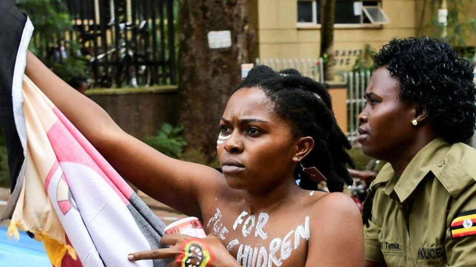 A Ugandan protester with the words "for the children" painted on her bare chest and holding a flag is detained by a police officer for protesting over corruption outside parliament in Kampala, Uganda - Monday 2 September 2024