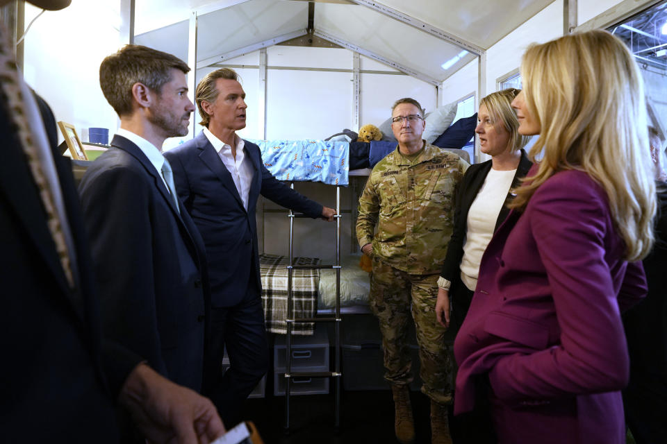 California Gov. Gavin Newsom, second from, left, talks with Amy King, founder and CEO of Pallet, in one the prototypes of the shelters her company makes, during a tour of the small homes displayed at a news conference where Newsom announced plans plans to build 1,200 small homes across the state to reduce homelessness, during the first of a four-day tour of the state in Sacramento Calif., on Thursday, March 16, 2023. (AP Photo/Rich Pedroncelli)