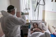 In this photo taken on Thursday, May 28, 2020, Father Yaroslav Rokhman, Ukrainian Greek Catholic Church priest, wearing protective gear to protect against coronavirus, blesses Galina Shamineva, 34, dying of cancer, at a hospice in Ivano-Frankivsk, Ukraine. Rokhman, a priest in the Ukrainian Greek Catholic Church, is pleased to be able to return to performing one of a cleric's most heartfelt duties. As the coronavirus pandemic's grip on Ukraine slowly recedes, priests received permission on May 22 to again hold services and visit the sick. (AP Photo/Evgeniy Maloletka)