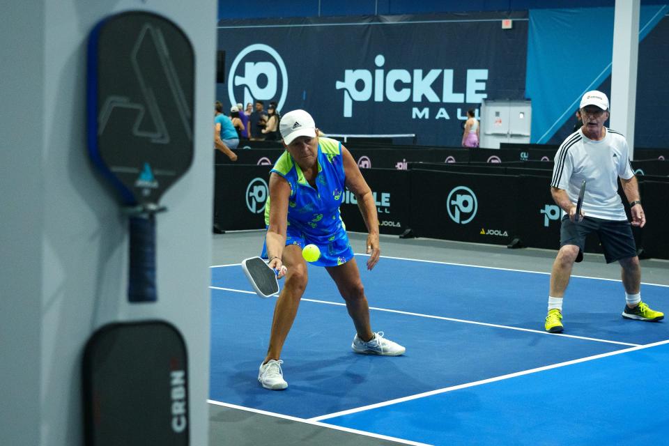 Paddles hang on the wall as Linda Ellis goes after the ball during a pickleball game at Picklemall at Arizona Mills on Aug. 5, 2023, in Tempe.