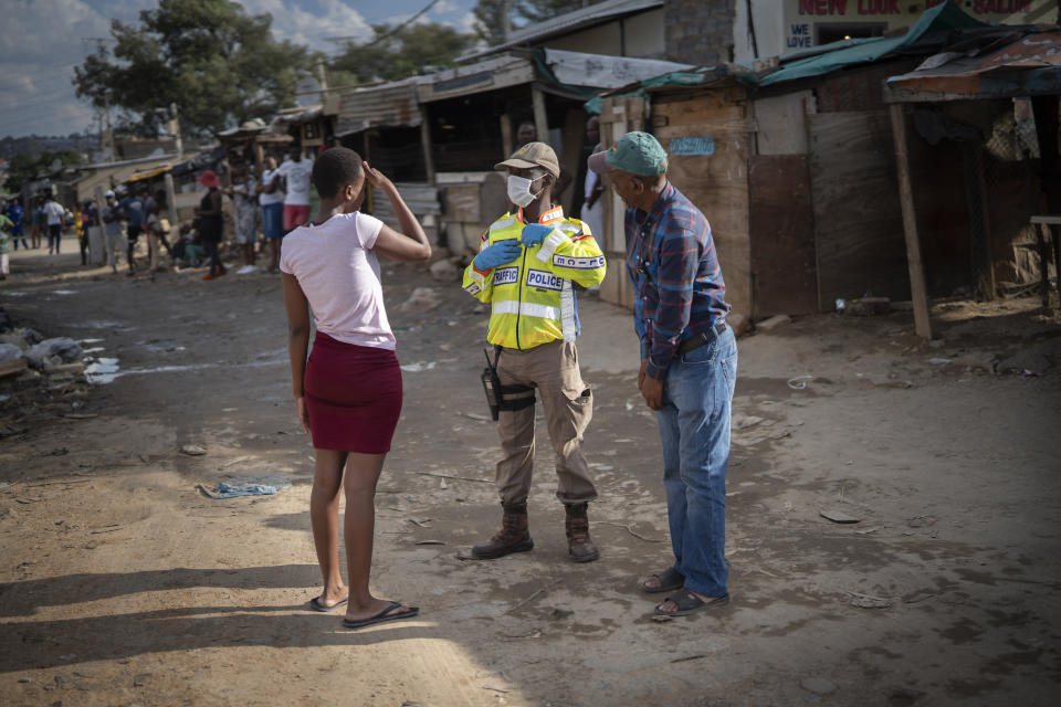 A South African police officer speaks to residents of the densely populated Alexandra township east of Johannesburg Friday, March 27, 2020. South Africa went into a nationwide lockdown for 21 days in an effort to mitigate the spread to the coronavirus, but in Alexandra, many people were gathering in the streets disregarding the lockdown. The new coronavirus causes mild or moderate symptoms for most people, but for some, especially older adults and people with existing health problems, it can cause more severe illness or death.(AP Photo/Jerome Delay)