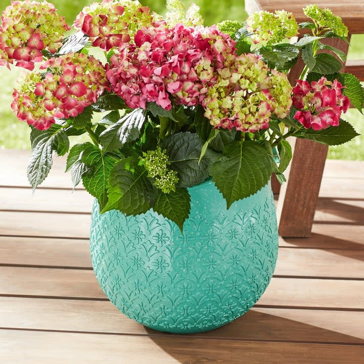 the round turquoise planter with flowers inside on a deck