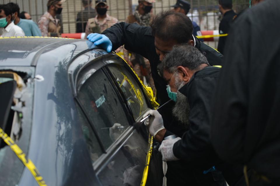 Members of Police Crime Scene Unit investigate around a car used by alleged gunmen at the main entrance of the Pakistan Stock Exchange building in Karachi on June 29, 2020. - At least six people were killed when gunmen attacked the Pakistan Stock Exchange in Karachi on June 29, with a policeman among the dead after the assailants opened fire and hurled a grenade at the trading floor, police said. (Photo by Rizwan TABASSUM / AFP) (Photo by RIZWAN TABASSUM/AFP via Getty Images)