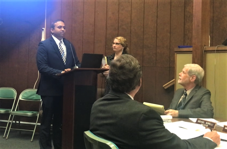 Summit Wellness LLC principal Kal Shah (standing, left) testifies Monday night before the Woodbury Heights Planning Board. Shah described his proposal to convert a former bank at 1002 Mantua Pike into retail cannabis store. His attorney, Heather Kumer, stands with him. The board unanimously approved the store. PHOTO: June 5, 2023.
