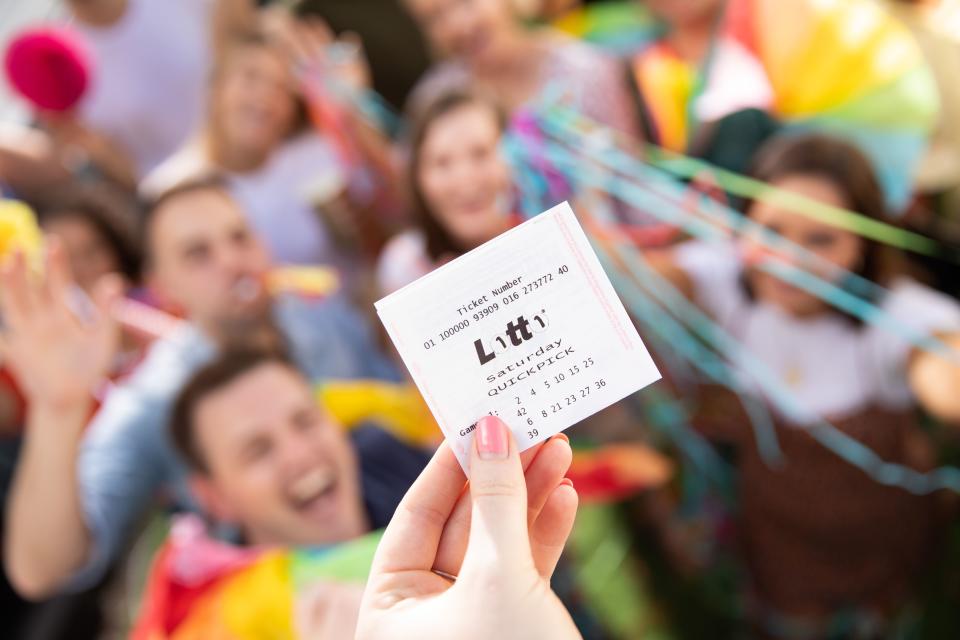 Winning Saturday Lotto ticket being held up in front of celebrating crowd. 