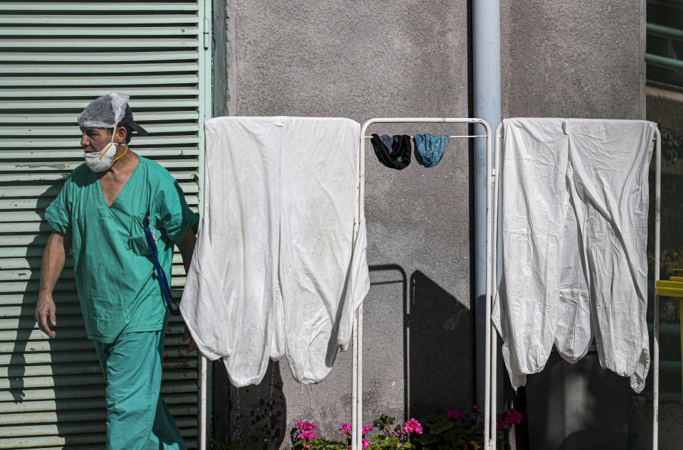 En esta imagen, tomada el 26 de mayo de 2020, un trabajador médico pasa junto a trajes de protección colgados al sol para que se sequen, en el hospital San José, en Santiago, Chile. (AP Foto/Esteban Félix)