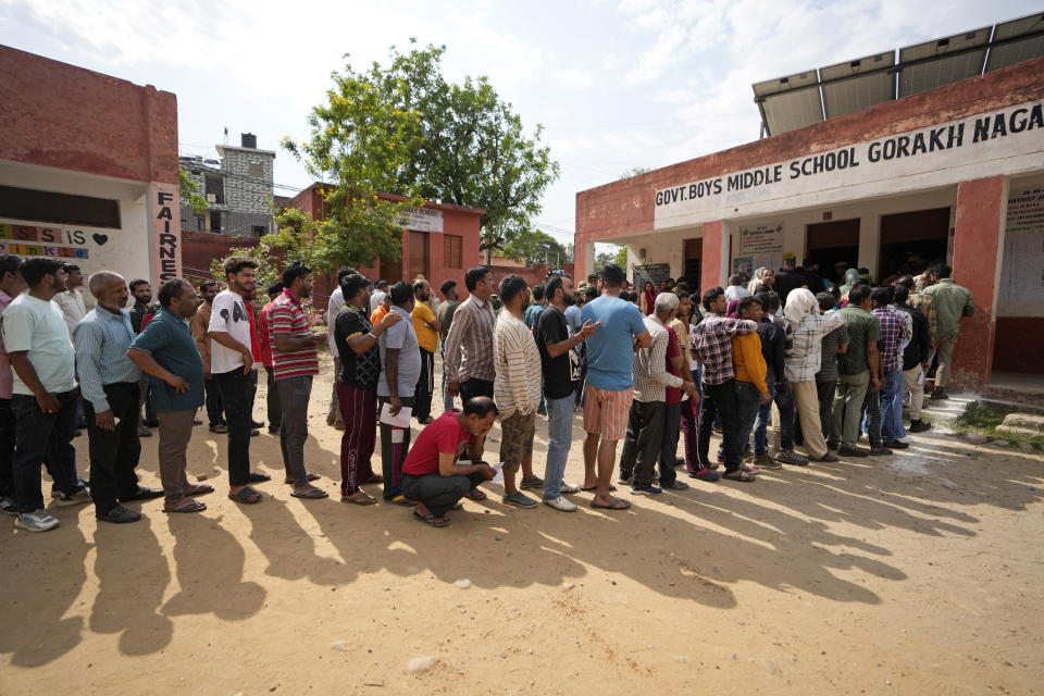 A man squats to rest as people queue up to vote during the second round of voting in the six-week-long national election in Jammu, India, Friday, April 26, 2024. (AP Photo/Channi Anand)