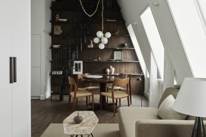 wood wall with exposed shelving, angled wall with large cut outs for windows with orb lighting fixture above dining table