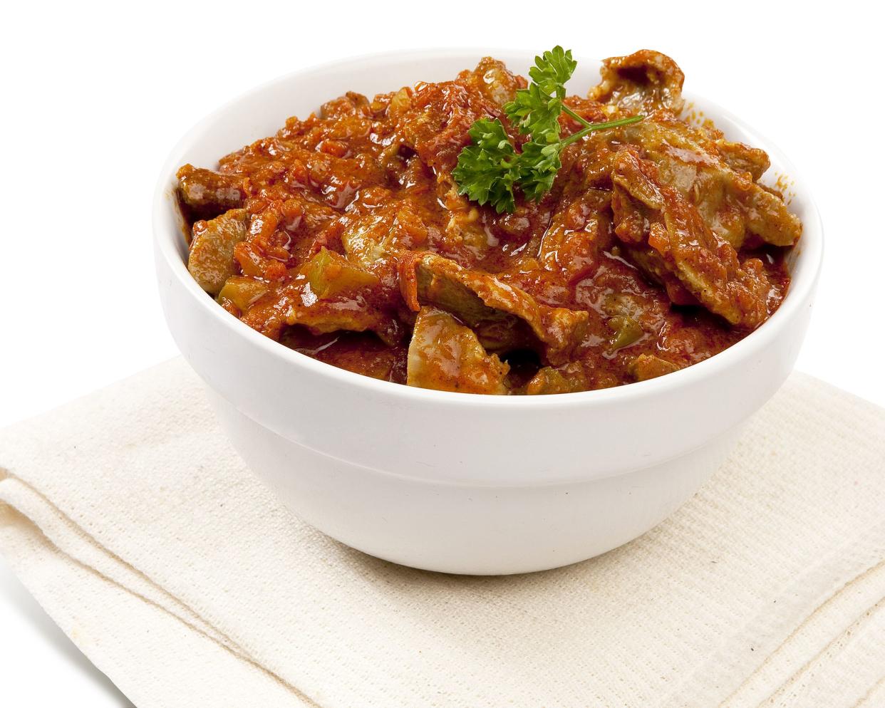 African-style braised chicken in peanut sauce (crock pot) in a white bowl on a napkin with a white background