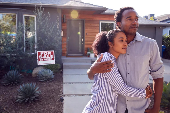 A mixed-race couple outside a home marked with a sign saying For Sale by Owner. (Getty Images)