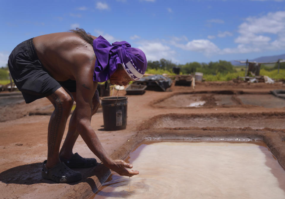 Kane Turalde reaches into a salt bed to examine the salt crystals on Friday, July 14, 2023, in Hanapepe, Hawaii. Climate change, air pollution and littering by tourists and visitors are all threats to this practice, but the 22 families who continue this tradition are fighting to keep these threats at bay and pass on this sacred practice to future generations. (AP Photo/Jessie Wardarski)