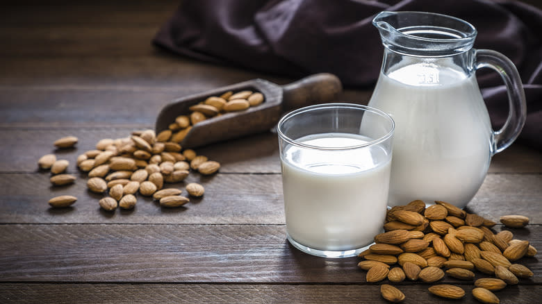 Almond milk in a pitcher next to almond nuts