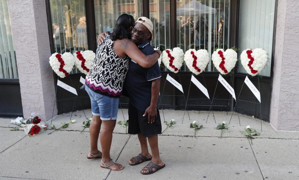 A man and a woman hug each other in front of wreaths displayed for the nine victims of a shooting in the Oregon District of Dayton, Ohio. Nine people died.