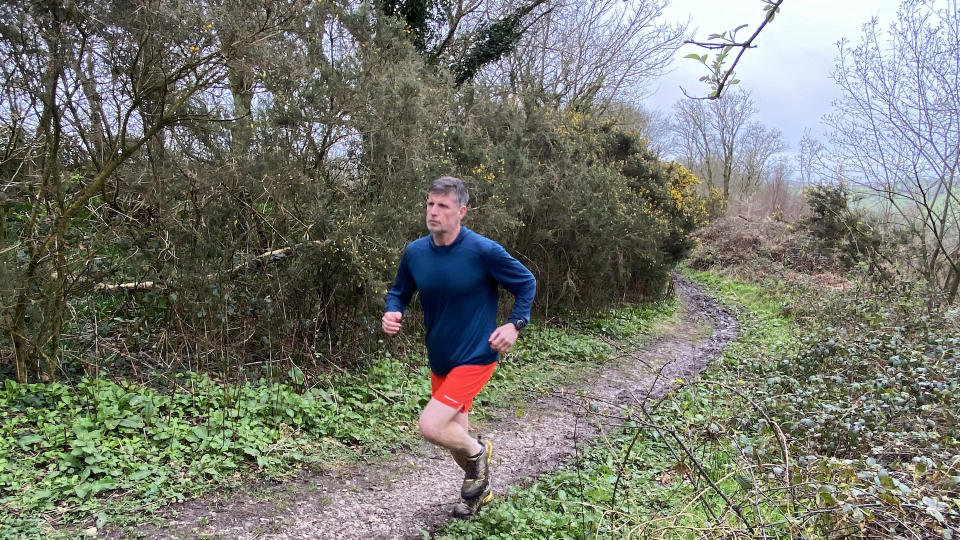 Man running on muddy trail wearing Smartwool Men's Active Mesh Hoodie