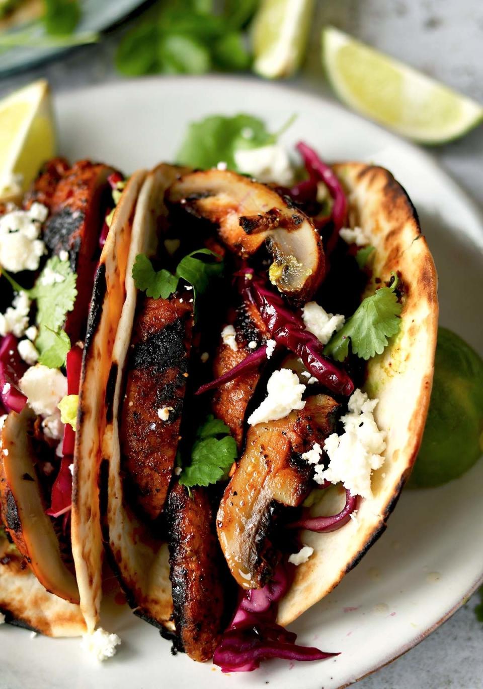 Two tacos filled with sliced mushrooms, cabbage, herbs, and cotija cheese