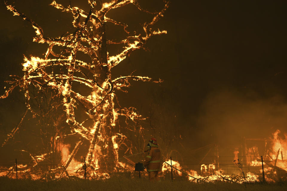 In this Saturday, Dec. 21, 2019, photo, NSW Rural Fire Service crew fight the Gospers Mountain Fire as it impacts a property at Bilpin, New South Wales state, Australia. Prime Minister Scott Morrison on Sunday, Dec. 22, apologized for taking a family vacation in Hawaii as deadly bushfires raged across several states, destroying homes and claiming the lives of two volunteer firefighters.(Dan Himbrechts/AAP Images via AP)