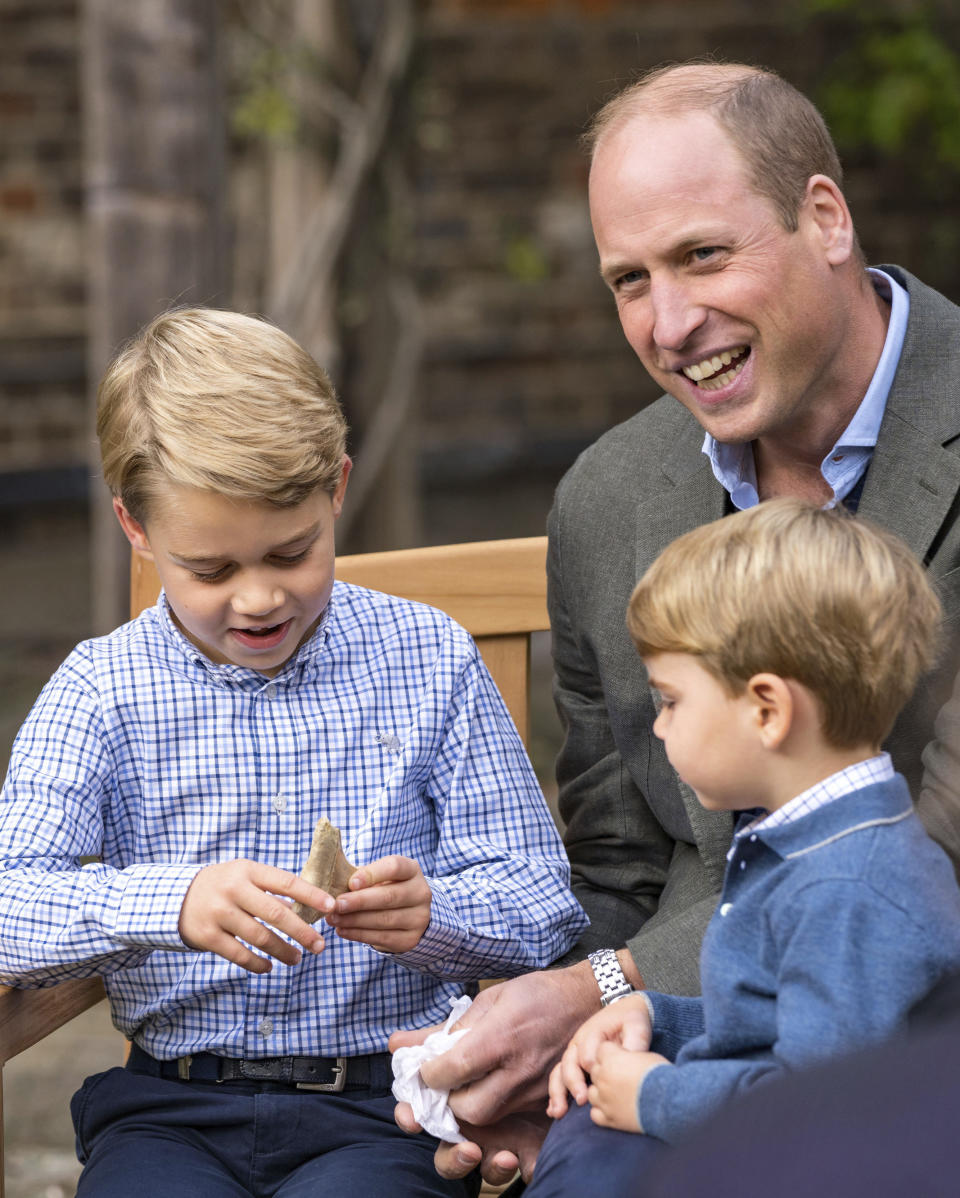 In this Thursday, Sept. 24, 2020 photo released by Kensington Palace, Britain's Prince William and Prince Louis react as Prince George holds the tooth of a giant shark given to him by Naturalist Sir David Attenborough in the gardens of Kensington Palace in London after Prince William joined Attenborough for an outdoor screening of his upcoming film - David Attenborough: A Life On Our Planet. (Kensington Palace via AP)