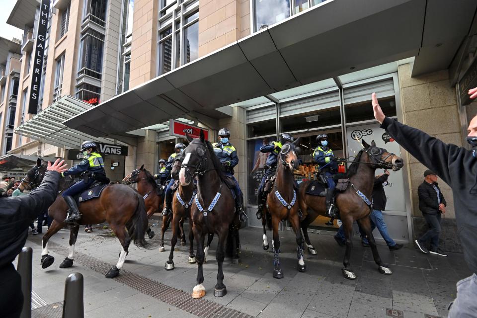 Police officers on horseback disperse protesters during a rally in Sydney on July 24, 2021, as thousands of people gathered to demonstrate against the city's month-long stay-at-home orders. (Photo by Steven SAPHORE / AFP) (Photo by STEVEN SAPHORE/AFP via Getty Images)