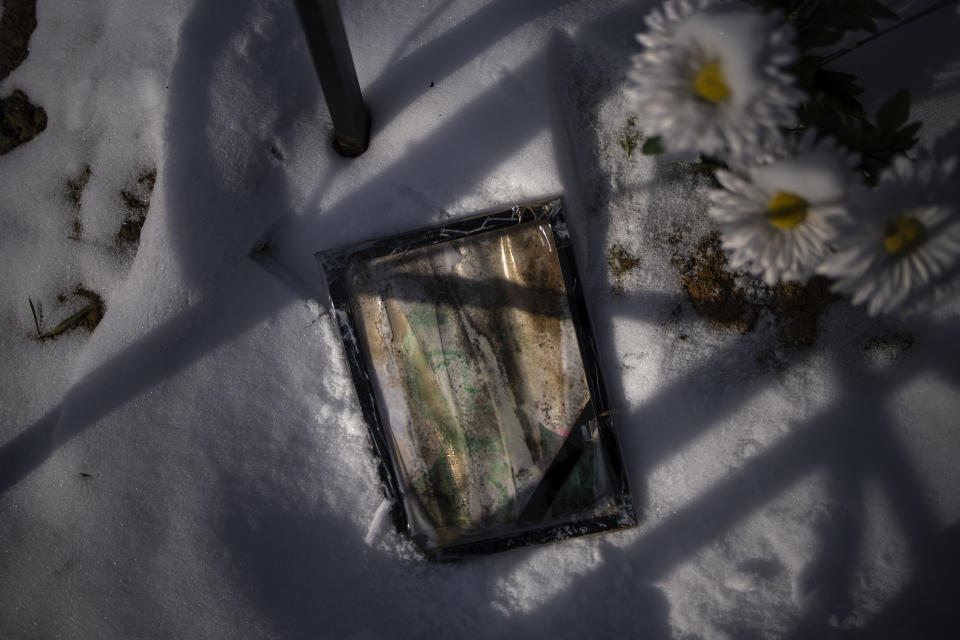 A worn-out portrait of Oleksandr Gryhorovych, 59, lies next to his grave at a cemetery in Kyiv, Ukraine, on Thursday, Feb. 9, 2023. He was buried on May 22, 2022. (AP Photo/Emilio Morenatti)