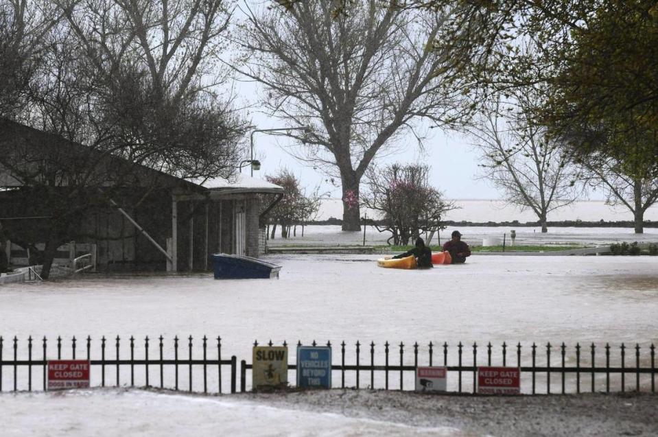 Two people make their way across their driveway with two kayaks in tow at a large home along Dairy Avenue about 4 miles south of Corcoran where flooding is re-creating the historic Tulare Lake. Photographed Wednesday, March 22, 2023 near Corcoran, California.