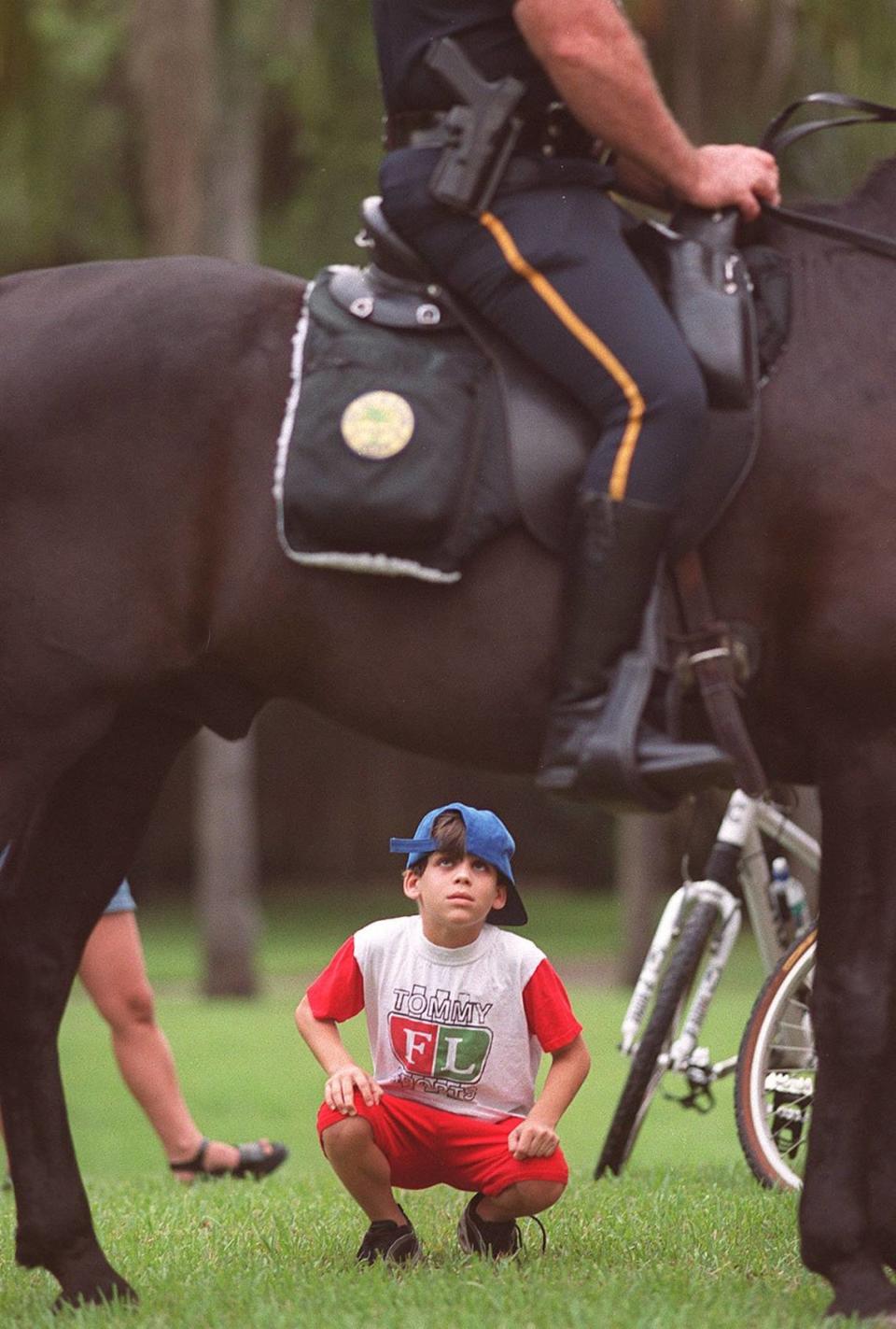 En esta foto de 1999, Ilia González, de nueve años, de Coral Gables mira al oficial de policía de Miami Manny Gómez montado en Shaker, un Tennessee Walker. Shaker, miembro de la patrulla montada desde 1992, acompañó a agentes de las ciudades de Miami, West Miami, Coral Gables y Miami-Dade en el Edmund P. Cooper Park para la National Night Out.