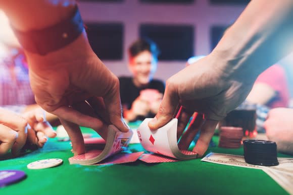 A man's hands shuffle a deck of cards on a green felt-covered table