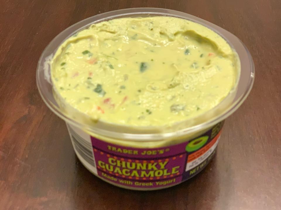 open pink and clear tub of trader joe's chunky guacamole with greek yogurt on wood table