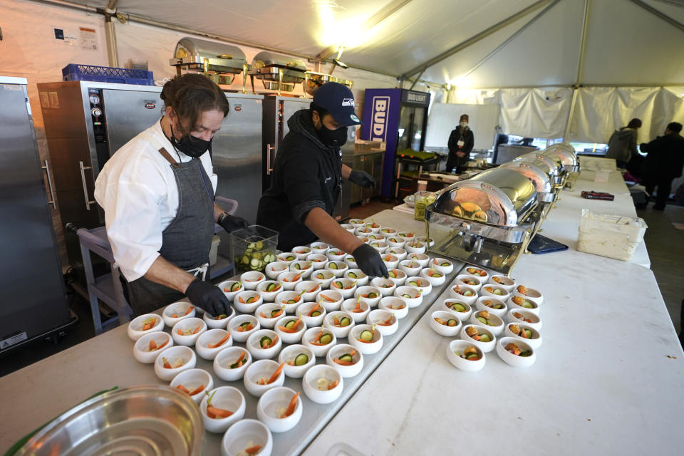 Jason Wilson, left, a chef at The Lakehouse, a restaurant located in Bellevue, Wash., and sous chef Demetrius Parker, right, prepare dishes for the first course of a meal for diners in an outdoor tent set up on the turf at Lumen Field, Thursday, Feb. 18, 2021, in Seattle. Wilson and Parker were two of the chefs taking part in the inaugural night of the "Field To Table" event at stadium, which is home to the Seattle Seahawks NFL football team. The event will feature several weeks of dates that offer four-course meals cooked by local chefs and served at tables socially distanced as a precaution against the COVID-19 pandemic. (AP Photo/Ted S. Warren)