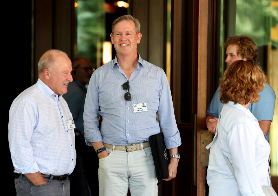 Comcast Chairman Michael Kavanagh stands with people as they arrive at the Sun Valley Lodge in Idaho.